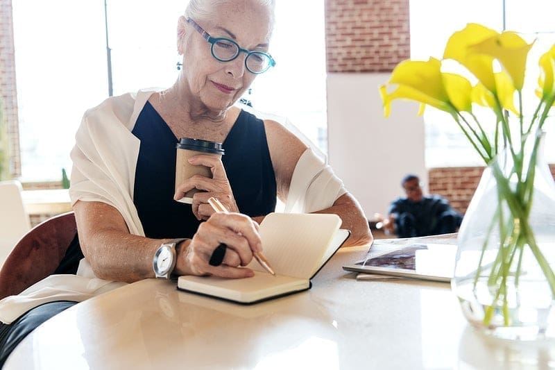 A Guide To Creating A Stellar Condo Association Newsletter 1 Older woman holding a coffee writing in a notebook - condo association newsletter
